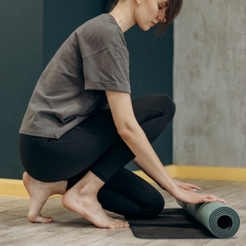 A young woman rolling out a yoga mat. She looks visibly unenthused. Or just very Zen. I can't tell.