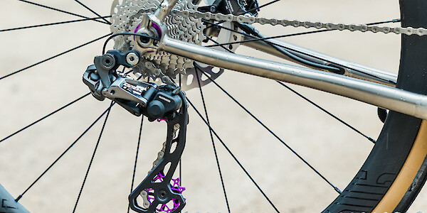 Cassette and rear derailleur detail on a titanium Bossi Grit gravel bike, showing the purple Garbaruk pulley wheels