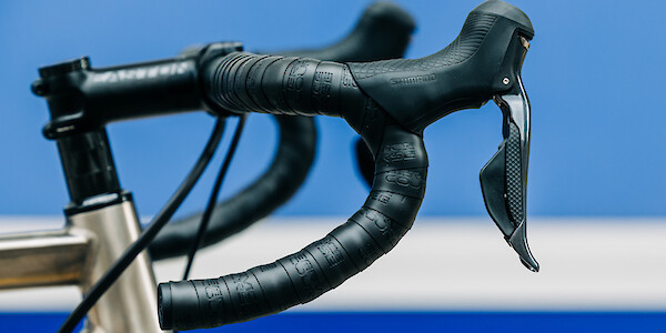 Handlebar and shifter detail on a titanium Bossi Strada road bike, against a segmented blue background