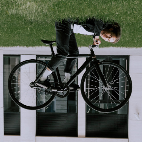 Upside-down picture of a young man lying on the lawn and balancing his bike on his feet