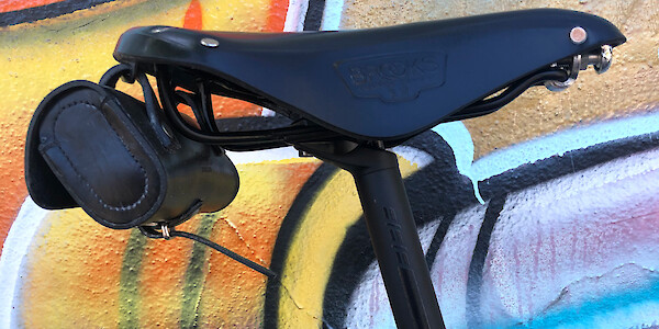 Close-up of a Brooks B17 saddle fitted to a custom Surly Midnight Special bike, against a wall of street art