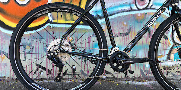 Rear wheel and drivetrain detail on a custom-built Surly Midnight Special bicycle, against a street art wall