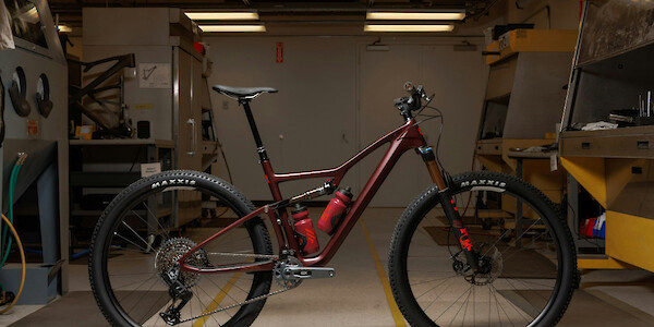 An Ibis Exie USA mountain bike in Blood Orange Burgundy, standing against a workshop background under overhead lights