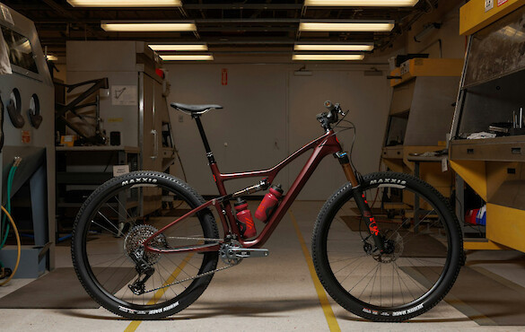 An Ibis Exie USA mountain bike in Blood Orange Burgundy, standing against a workshop background under overhead lights