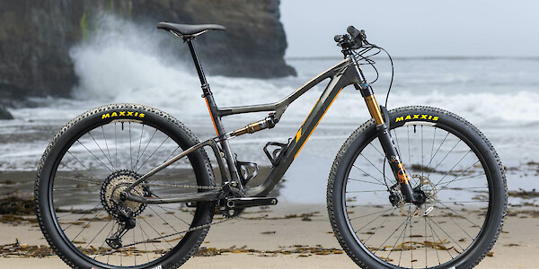Ibis Exie carbon mountain bike in Cheat-O Orange against a backdrop of raging surf and seaweed-strewn sand