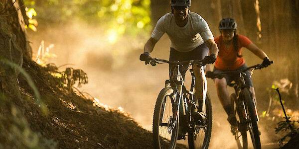 Mountain bikers carving up a forest trail, both riding Ibis Exie carbon mountain bikes, looking pretty stoked