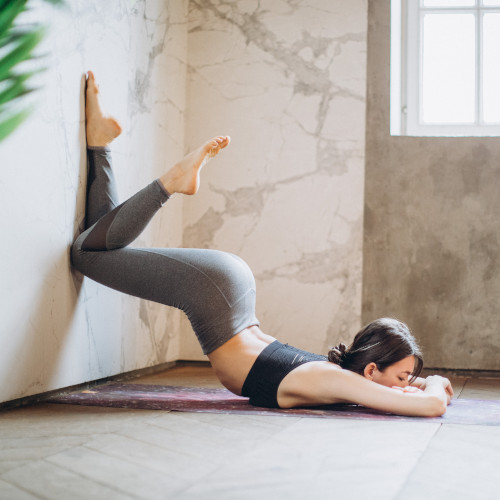 A woman in yoga gear, posing with her legs against a wall and her upper torso on the ground. She is in a graceful s-shape, though it looks like a back injury waiting to happen.