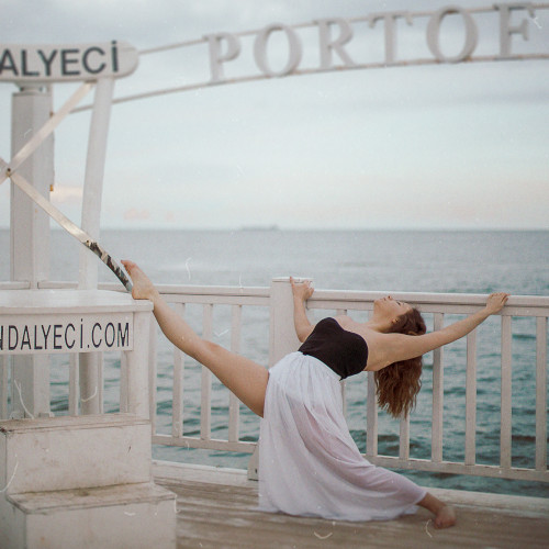 A woman in a black bustier and white top, doing a diagonal splits move on a jetty. It's less complicated than it sounds.