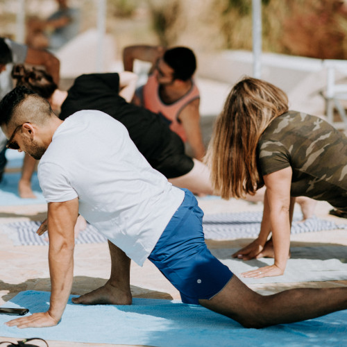 An outdoor yoga class with men and women in various stages of a hip flexor stretch.
