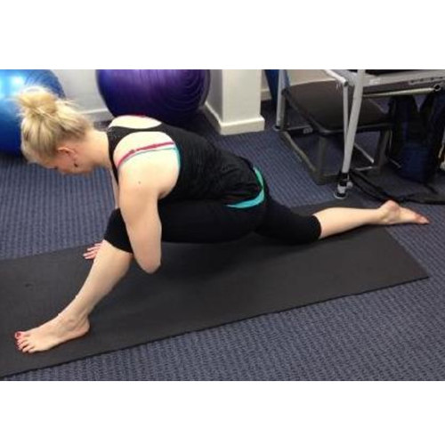 Remedial massage therapist Holly Hicks, positioned on a mat, demonstrating a hamstring stretch