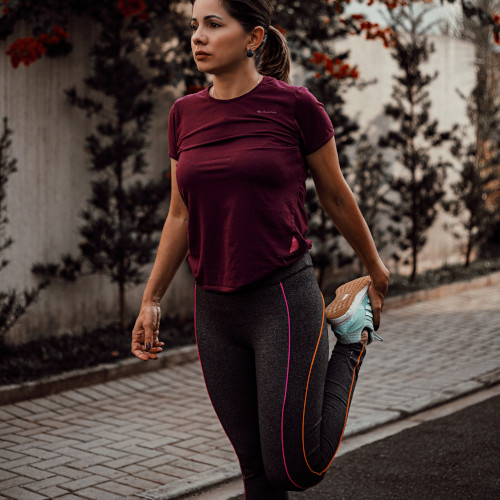 A woman outside wearing running gear, stretching her quadriceps. She looks preoccupied.