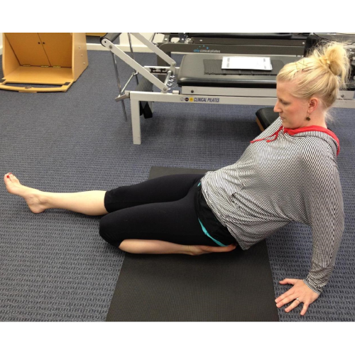 Remedial massage therapist Holly Hicks, on a mat, demonstrating a quadriceps stretch