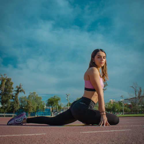 An athlete on the track, sitting in a glute stretch position and looking at the camera.