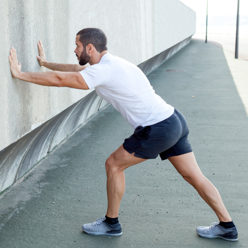 A man leaning against a concrete wall, performing a calf stretch.