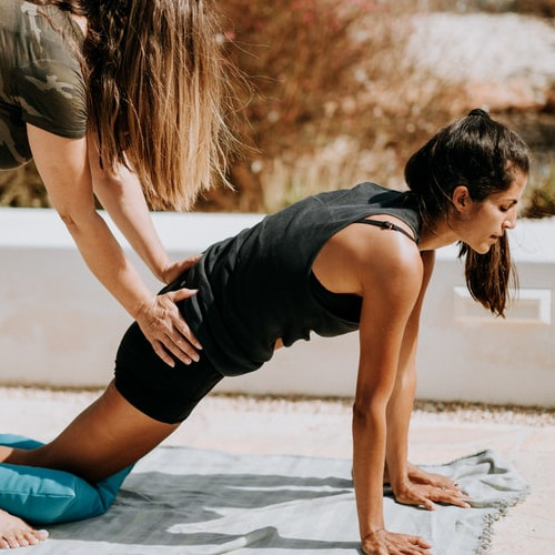 A woman doing a hip flexor yoga stretch, another woman assisting her with her hip position.