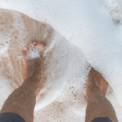 A man's feet, shot from above, in a foamy surf.