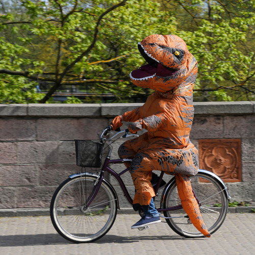 A person in a dinosaur suit riding a bicycle.