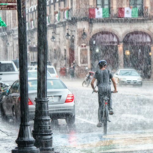 A cyclist riding through a city street in a torrential downpour.