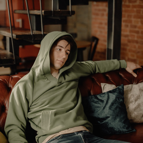 A young man in a hoodie, sitting on a couch and staring into space.