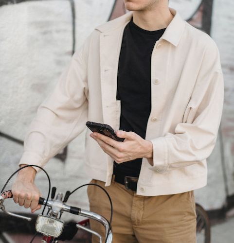 A young man holding a bicycle by the bars with one hand and checking his phone with the other.