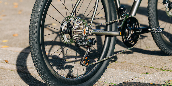 Detail of the drivetrain on a custom-built Bossi Grit SX titanium gravel bike, with Shimano GRX components plus orange Garbaruk jockey wheels