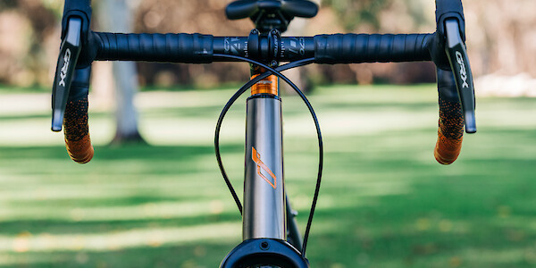 A custom-built Bossi Grit SX titanium gravel bike, viewed from the front to see the hand-painted headtube detail and matching orange acccents.