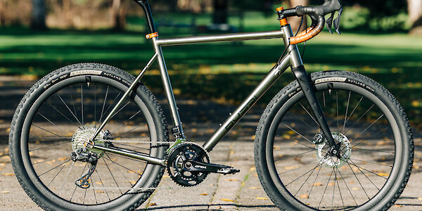 Custom-built Bossi Grit SX titanium gravel bike, against a park backdrop