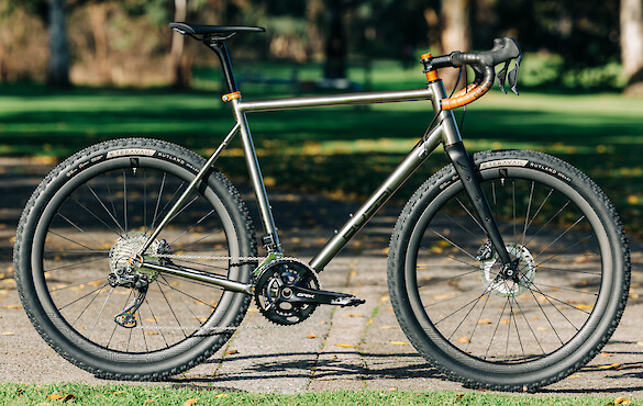 Custom-built Bossi Grit SX titanium gravel bike, against a park backdrop