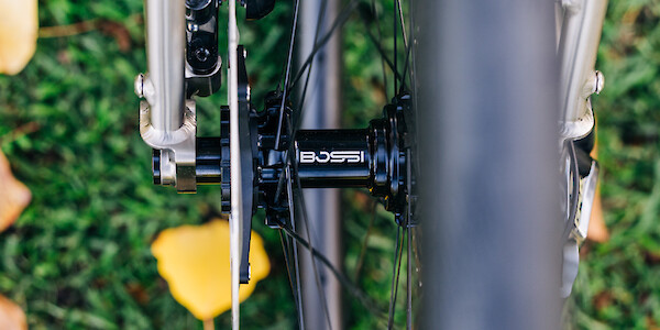Detail of a Bossi hub on a Bossi wheelset, fitted to a custom-built Bossi Grit SX titanium gravel bike, shot from above against a grassy backdrop