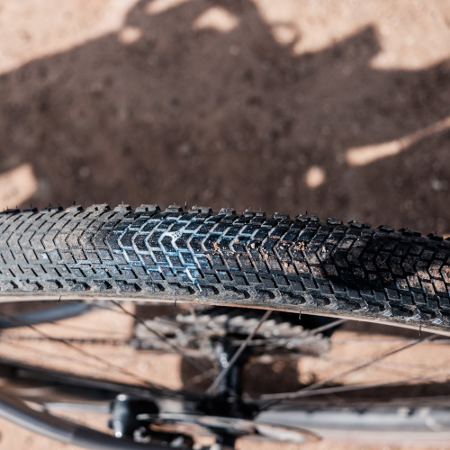 A gravel tyre which has been punctured; sealant is leaking through the tread. Viewed from above on a dirt road.