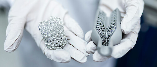 A person holding two lumps of material in their gloved hands, one metal, one three-D printed