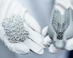 A person holding two lumps of material in their gloved hands, one metal, one three-D printed