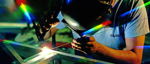 A welder working on a piece of metal, light refracting into rainbows around him