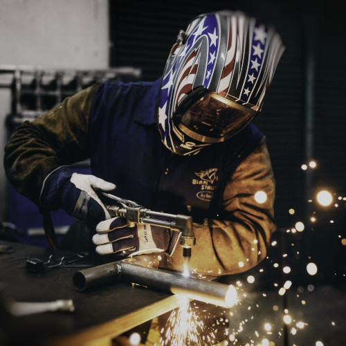 A welder wearing a stars and stripes face mask, working on some metal tubing