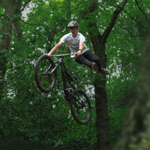 A young man mid-air, performing a trick on a mountain bike in a forest