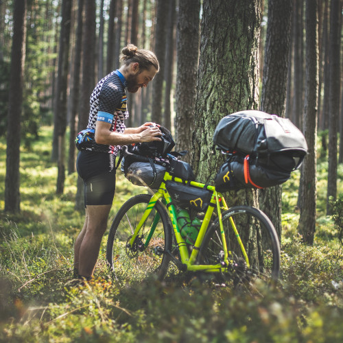 A bearded young man in the forest next to his bike, examining his bikepacking bag.