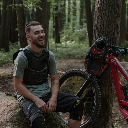 A mountain biker sits in the forest next to his bike, laughing.