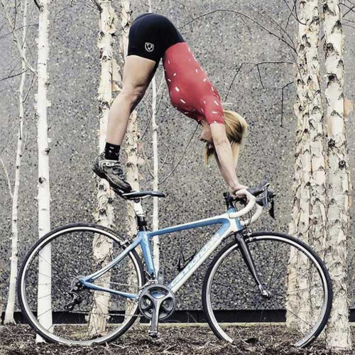 A woman does a yoga pose on top of a bicycle, in a forest.