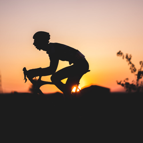 A road cyclist riding his bike, silhouetted against a sunset.