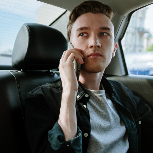 A young man on the phone in the back of a taxi, looking out the side window.