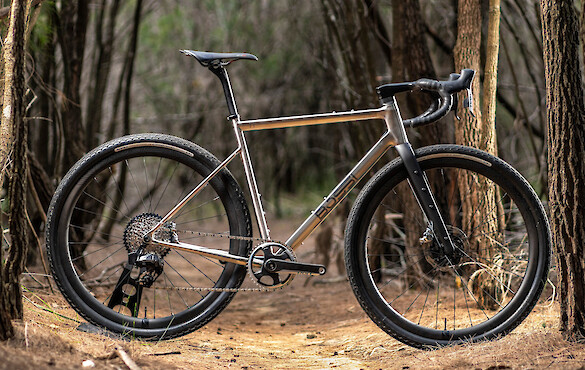Bossi Grit SS titanium gravel bike, photographed from the side in a forestry area.