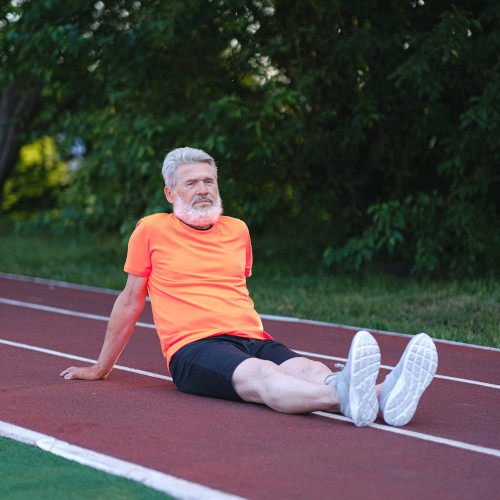 An older man sitting on a running track, looking despondent.