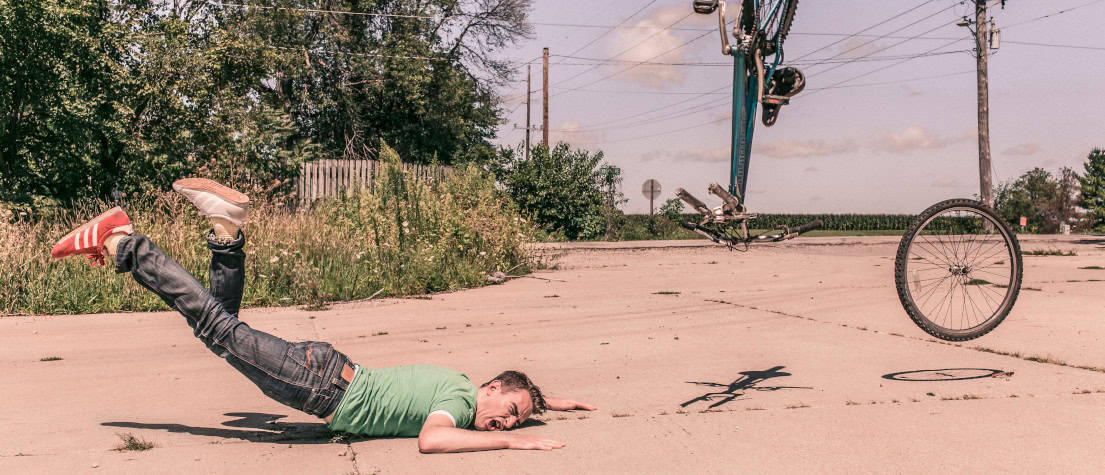 A man crashing to the ground during a bike accident, his bicycle flying off in pieces