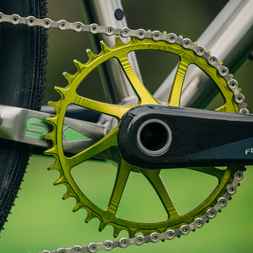 Drivetrain detail of a green Garbaruk chain ring, fitted to a titanium gravel bike