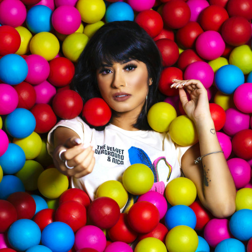 A woman lying against a backdrop of coloured balls, reaching her hand out to the camera.