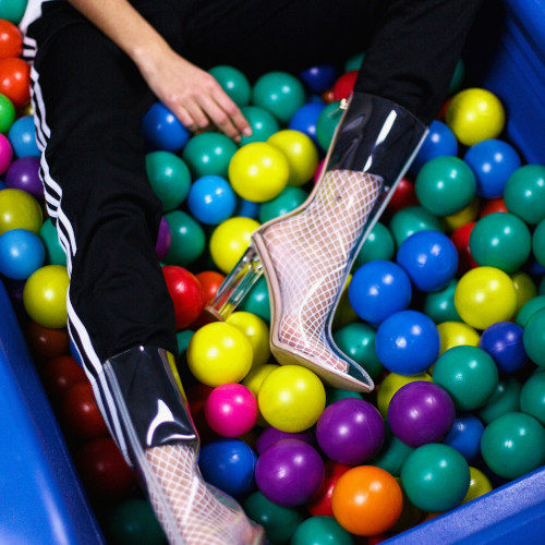 A woman's legs as she lies in a ball pit. She is wearing black tracksuit pants, and, for some reason, transparent boots.