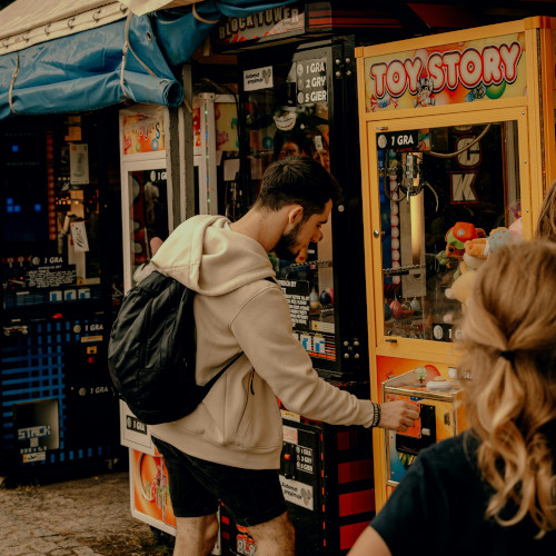 A bearded young man at a fun fair, putting money in a claw machine called Toy Story.