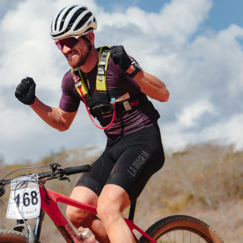 A mountain biker during a race, grinning with his fists raised in triumph.