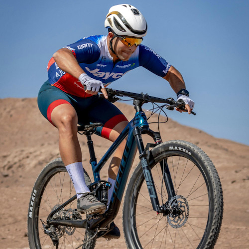 A mountain biker in an arid environment, mid-jump on a dual-suspension bike.