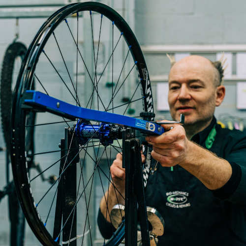 A professional bicycle mechanic checking the spoke tensions on a wheel at Bio-Mechanics Cycles & Repairs in South Australia.